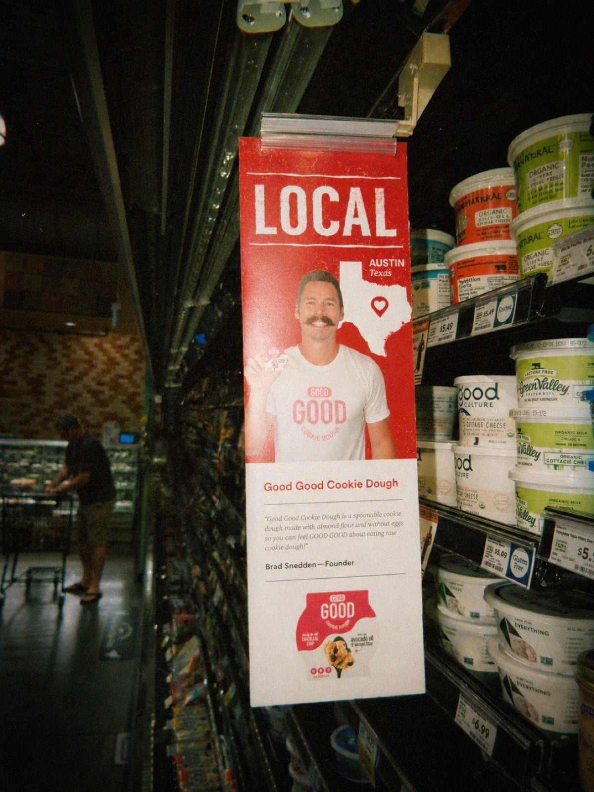 Brad in a GOOD GOOD Cookie Dough shirt next to the LOCAL Austin Texas endcap inside Whole Foods