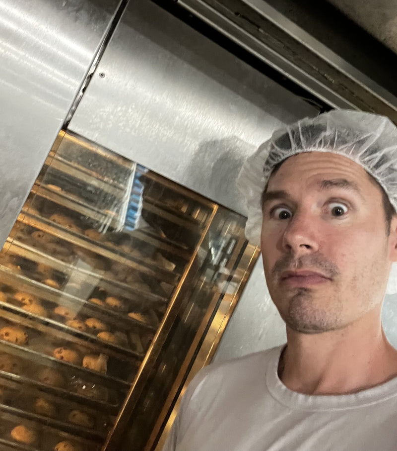 Brad in a hairnet next to oven racks of cookies in production