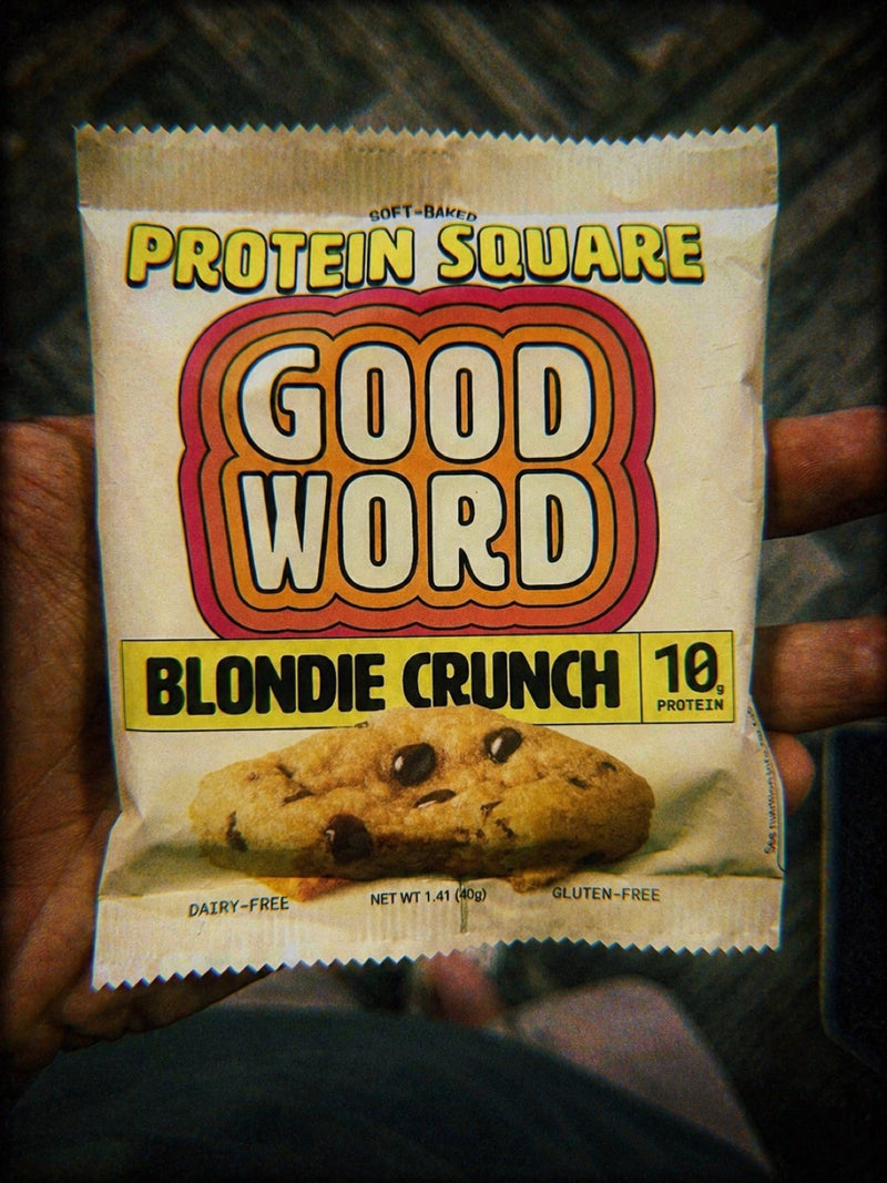 Hand holding a GOOD WORD Soft-Baked Protein Square Blondie Crunch package, 10g protein, dairy-free, gluten-free