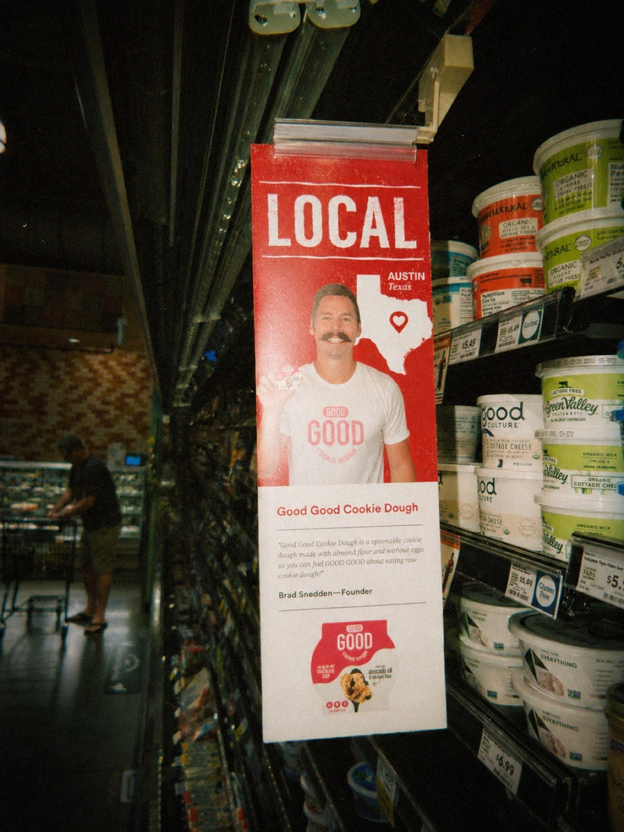 Brad in a GOOD GOOD Cookie Dough shirt next to the LOCAL Austin Texas endcap inside Whole Foods