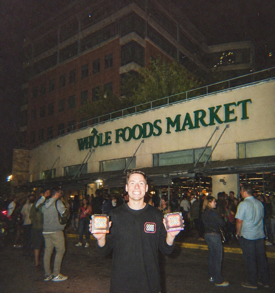 Brad in a GOOD GOOD hoodie holding two boxes of cookies outside the Whole Foods Market on launch night, crowd gathered